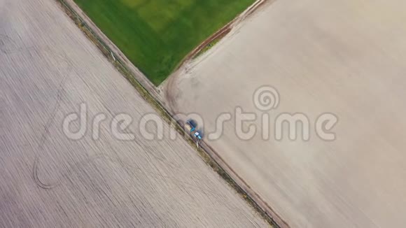 一辆拖拉机沿着一片绿色的田野在公路上行驶初秋农场工作高空俯视图视频的预览图