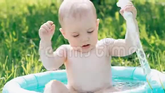 夏天小男孩在充气游泳池里游泳和玩喷水视频的预览图
