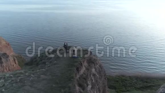 瑜伽宗教莲花姿势的瑜伽男女坐在海边的悬崖上沉思视频的预览图