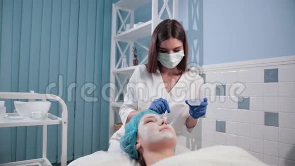护士医生给女性做面部按摩用刷子做白色面膜视频的预览图