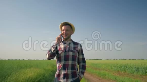 在手机上聊天时心情愉快农民戴着草帽穿着格子衬衫走在乡间小路上视频的预览图