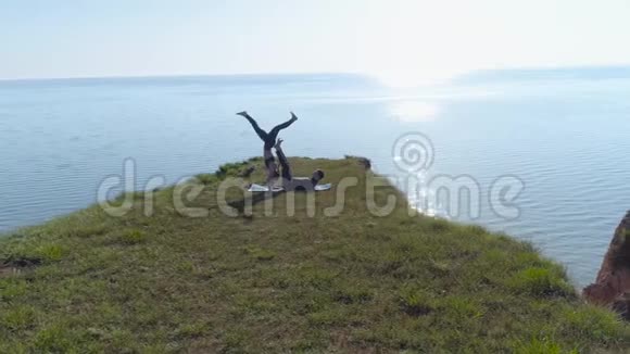 阿克罗伊加强壮的瑜伽男性和灵活的女性在靠近海洋的山上进行配对平衡练习视频的预览图
