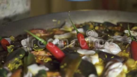 厨师烹饪西班牙海鲜饭与红辣椒和新鲜海鲜在锅里关闭传统西班牙视频的预览图