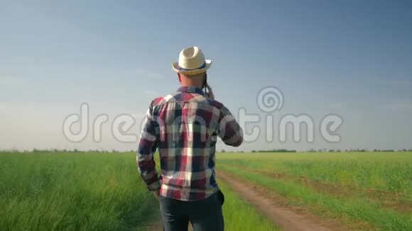 快乐的农夫戴着草帽穿着格子衬衫在一部手机上聊天在乡间散步时心情愉快视频的预览图