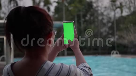 晚上女士在度假村游泳池用智能手机用绿色屏幕拍照视频的预览图