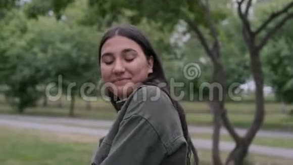 年轻的时髦的黑发女孩留着一个便携式扬声器在公园里随着音乐翩翩起舞视频的预览图