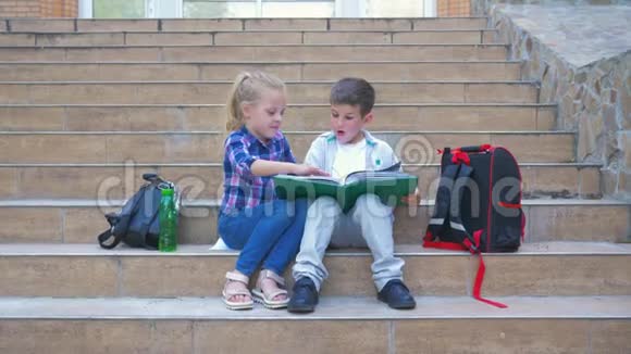 小学学生背着背包坐在台阶上在户外休息时翻阅一本书视频的预览图