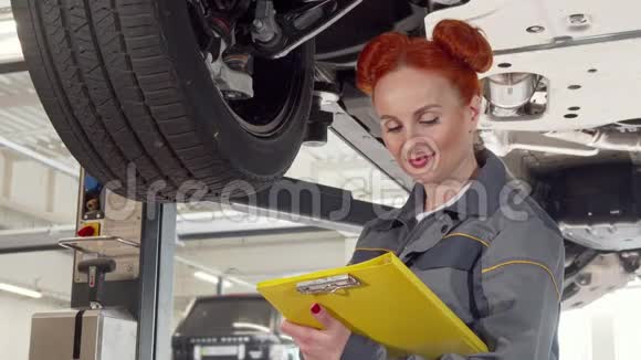 女汽车修理工在电梯上检查汽车的车轮在剪贴板上做笔记视频的预览图
