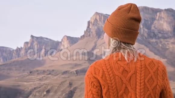 从后面看一个穿着橙色毛衣和帽子的旅行女孩在户外看台上背景是史诗般的背景视频的预览图