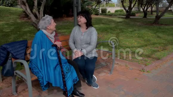 女志愿者和老妇人坐在城市公园的长椅上谈话视频的预览图