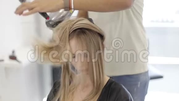 一位男理发师在一家现代化的美容店里烘干长发金发吹风机视频的预览图