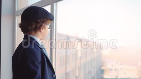 穿着商务服领带和帽子的小男孩从商务办公室的窗户往外看视频的预览图