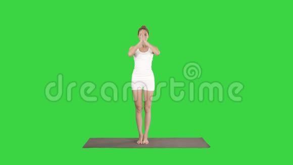 漂亮的女孩站在平衡瑜伽姿势加鲁达萨纳年轻女子鹰瑜伽姿势在绿色屏幕上视频的预览图