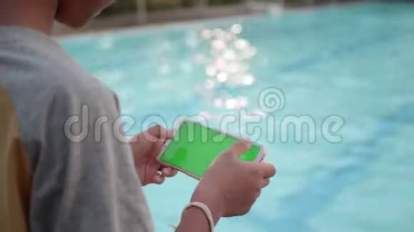 儿童手使用智能手机在线游戏绿色屏幕放松附近游泳池在晚上视频的预览图