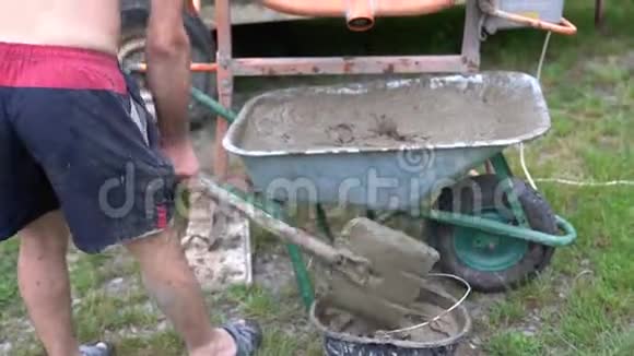 青年工人从手推车中收集混凝土溶液放入桶中视频的预览图