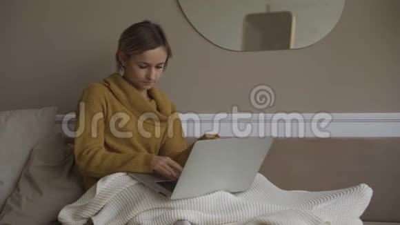 学生在家使用笔记本电脑躺在沙发上的毯子下使用电脑锯线进行在线咨询人和人视频的预览图