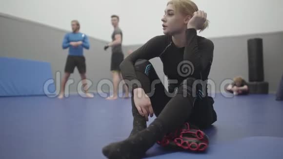 肖像运动女子坐在健身房的地板上休息后训练饮用水从瓶子金发女郎视频的预览图