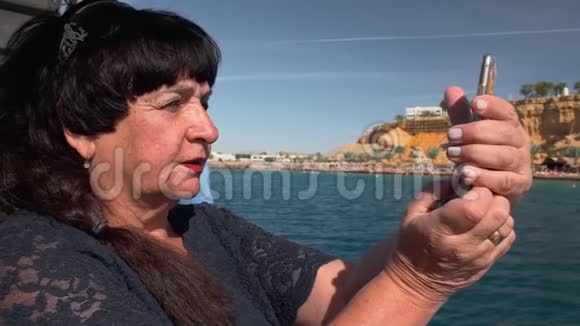 船上的老年女性快乐成人游客使用移动智能手机相机拍摄热带岛屿全景照片视频的预览图