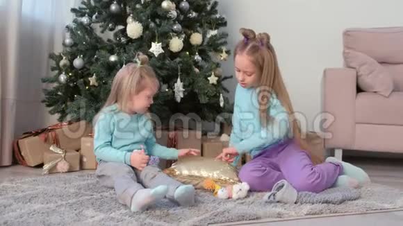 两个女孩的姐姐在靠近圣诞树的枕头上用亮片画手指视频的预览图
