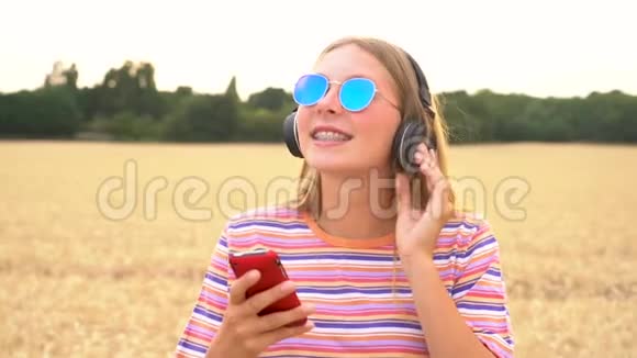 金发少女少女年轻女子用手机和无线耳机听音乐视频的预览图