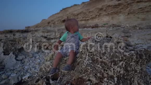 日落时坐在海边的石头上孩子说话坐立不安视频的预览图