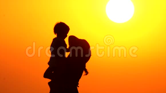 有孩子的优雅母亲孩子在母亲手中的日落背景日落时带孩子的父母剪影视频的预览图