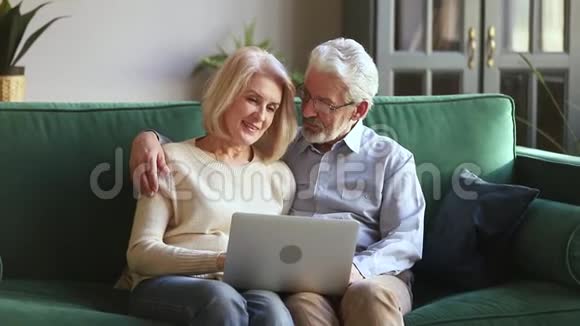 快乐的老两口在家里一起拥抱使用笔记本电脑视频的预览图