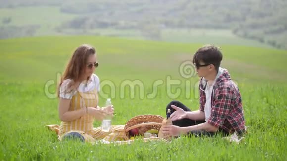 一对年轻夫妇穿着鲜艳的衣服坐在一片明亮的绿色草地上看着锅里的东西视频的预览图