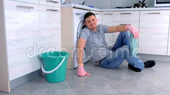 戴着橡胶手套的快乐微笑的男人从厨房地板上的清洁中休息视频的预览图