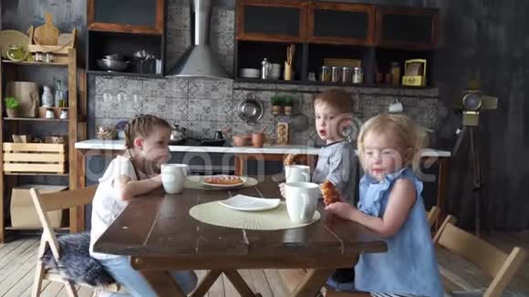 家庭晚餐三个孩子在厨房的桌子上吃面包和喝茶视频的预览图