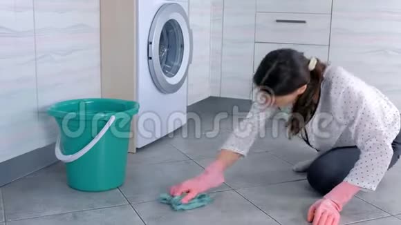 穿着粉红色橡胶手套的疲惫的女人用一块布洗和用力摩擦厨房地板上的污渍地板上的灰色瓷砖视频的预览图