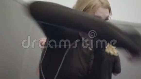 职业年轻漂亮的金发女郎戴着黑色拳击手套在镜头前拳击视频的预览图