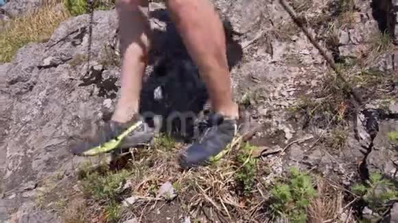 在这个框架中一个穿着运动鞋的人的腿在陡峭的岩石斜坡上下降视频的预览图