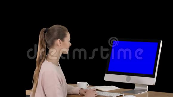 女孩坐在电脑显示器前看着一些微笑的蓝色屏幕模拟显示阿尔法频道视频的预览图
