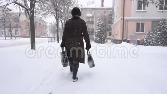 一个女人拿着袋子在一个下雪的城市里买东西这是雪冬天新年礼物慢动作视频的预览图
