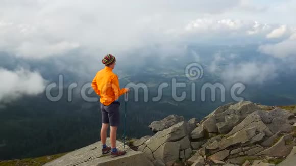 上面穿着一件漂亮夹克的徒步旅行者一个游客从山顶看云和风景视频的预览图