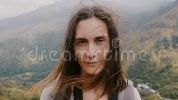 年轻位年轻快乐的旅游女性的特写肖像她带着背包在令人难以置信的山地背景下头发上随风飘荡视频的预览图