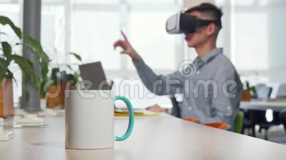 桌上放着一杯咖啡男人在后台工作时用3dvr杯视频的预览图