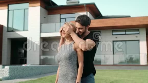 英俊的男人在房子附近闭上女人的眼睛站在别墅附近的一个吃惊的女人视频的预览图
