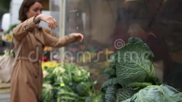 漂亮的年轻女人在市场上买蔬菜年轻女子手里拿着卷心菜在市场上妇女视频的预览图