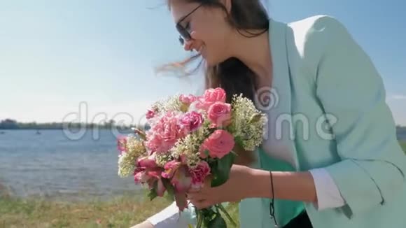 喜笑颜开的花店小姑娘戴着墨镜在河边的草地上收集一束束美丽的鲜花视频的预览图