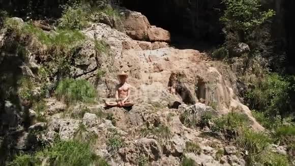一个戴着帽子的人坐在莲花的位置上坐在悬崖的边缘沉思着无限空中观景4k视频的预览图