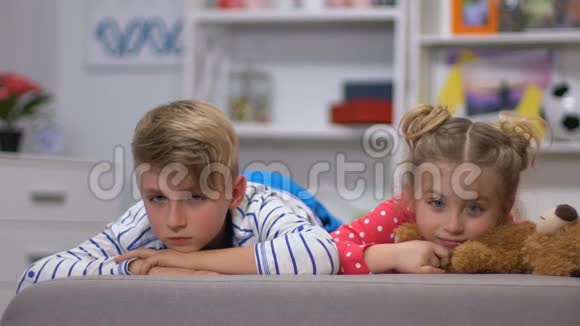 孩子们躺在沙发上看着摄像机男孩看着妹妹照看后感到疲倦视频的预览图