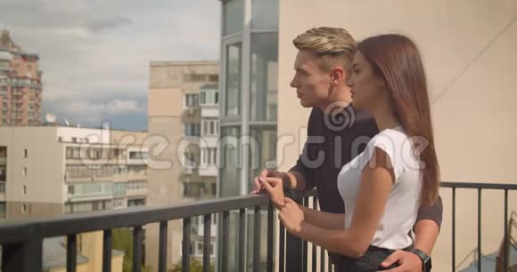 一对年轻可爱的白种人夫妇的特写肖像他们站在房子的阳台上看着美丽的视频的预览图