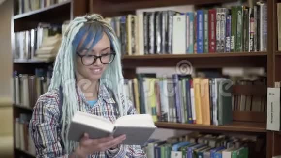 戴眼镜的嬉皮士女人带着可怕的笑容在图书馆看书视频的预览图