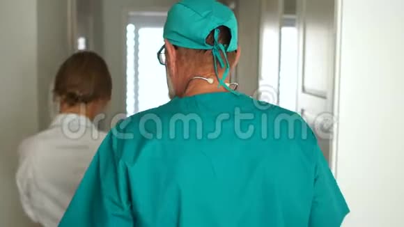 两名医生正沿着诊所的走廊走进办公室穿着医用礼服的男人和女人背面视频的预览图