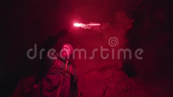 洞穴黑暗中的石头上有红色燃烧信号的人剪影极端的旅游理念视频的预览图