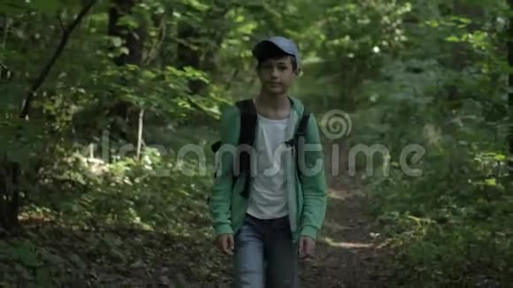 一个带背包的带着帽子的旅行男孩穿过树林四处张望视频的预览图