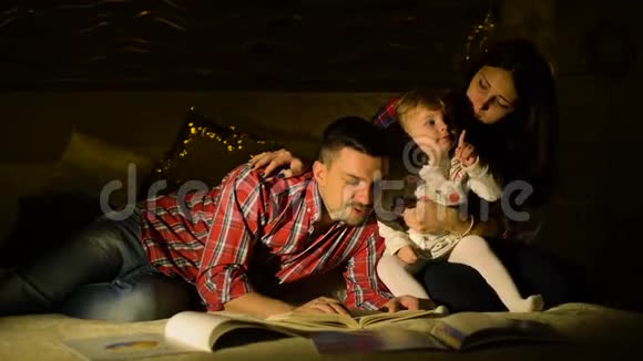 幸福的家庭和蹒跚学步的女儿晚上在床上看书视频的预览图