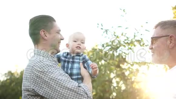 老灰头发的父亲他英俊的儿子和可爱的孙子的肖像在夕阳中笔直地微笑着视频的预览图